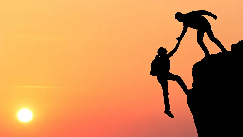 En person hjelper en annen opp en bratt fjellskrent